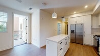This well-appointed single-floor unit offers a clean, contemporary design throughout, characterized by crisp white walls, light wood-style flooring, and black hardware accents that provide a modern contrast.

The kitchen is a standout feature, boasting an abundance of white shaker-style cabinetry that extends to the ceiling, complemented by open shelving for display or storage. A classic white subway tile backsplash lines the walls, while a suite of stainless steel appliances — including a French door refrigerator with water dispenser, a gas range with overhead microwave, and a dishwasher — delivers both style and full functionality. A central island with a white quartz countertop and built-in drawers provides additional prep space and storage. Pendant lighting overhead adds warmth and definition to the area.

The open layout connects the kitchen to the main living area, which benefits from recessed lighting and access to an exterior door, allowing natural light to filter into the space. A dedicated laundry closet houses a stacked washer and dryer, offering convenient in-unit functionality.

The bathroom is finished with large-format tile flooring, a white vanity with an undermount sink, a full-width mirror, and clean, neutral finishes throughout. The bedroom features neutral carpet, a bright window with blinds, and a serene, light-filled atmosphere ideal for rest.