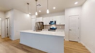 Located at 2121 N 99th Ave in Phoenix, AZ, this well-designed one-bedroom, one-bathroom unit offers a clean, modern aesthetic throughout its single floor of living space. The open-concept kitchen and living area serves as the heart of the home, anchored by a generous white quartz island with an undermount sink and elegant pendant lighting overhead. Crisp white cabinetry extends to the ceiling, complemented by a neutral tile backsplash and a full suite of stainless steel appliances, including a refrigerator, electric range, and microwave. Light wood-tone flooring flows seamlessly throughout the entire unit, enhancing the bright, airy atmosphere. The living area features a ceiling fan and a sliding glass door that opens to a private balcony, allowing for natural light and outdoor access. The bedroom is a comfortable retreat with a ceiling fan, a window with blinds, and direct access to a walk-in closet outfitted with multi-tier shelving and hanging rods. The bathroom is appointed with white cabinetry, a quartz vanity, and a full tub-shower combination. A dedicated laundry area houses a full-sized side-by-side washer and dryer with overhead shelving for added convenience.