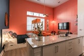 Located at 1099 Boulevard SE in Atlanta's dynamic Grant Park neighborhood, this single-floor studio makes a bold design statement through its striking use of color and thoughtful layout. The living area is defined by vivid orange accent walls that rise to impressively tall ceilings, creating a dramatic yet energetic atmosphere. Natural light streams in through large windows fitted with horizontal blinds, while a woven pendant lamp and curated wall art add warmth and personality. A striped area rug anchors the living space, which also features a built-in wall-mounted shelving unit and a dedicated workspace area.

The kitchen is efficiently designed with crisp white cabinetry, granite countertops, a subway tile backsplash, and a full suite of stainless steel appliances including a refrigerator, electric range, microwave, and dishwasher. A granite-topped island provides additional prep and casual dining space. Light hardwood-style flooring flows consistently throughout the entire unit, lending a cohesive, clean look.

The bathroom is well-finished with granite countertops, modern white cabinetry, an undermount sink, and a tiled shower-tub combination. Colorful artwork continues the space's lively character. A closet area with double doors provides practical storage. Overall, this studio offers a compact yet impressively styled living environment with high-impact design details throughout.