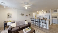Located in Lafayette, Louisiana, this single-floor residence offers seven bedrooms and four bathrooms across a well-designed, functional layout. The open-concept living and kitchen area serves as the heart of the home, where light hardwood-style flooring, crown molding, and a textured ceiling create a welcoming atmosphere. A ceiling fan with overhead lighting anchors the living room, which features large windows dressed with floor-to-ceiling gray curtains that allow generous natural light to fill the space. The kitchen is equipped with white cabinetry, white appliances, track lighting, and a peninsula-style breakfast bar with seating for multiple guests — ideal for casual dining and entertaining. The bedrooms are comfortably sized, each featuring ceiling fans, carpeted floors, and windows with blinds that provide natural light and outdoor views. The bathrooms are finished with tile flooring, white vanities with countertop sinks, and shower-tub combinations. A hallway and closet provide additional storage and connectivity throughout the home. The overall design is clean and neutral, with a cohesive color palette of whites and warm beiges that lends a bright, airy feel to every room. This residence offers a practical and comfortable multi-room floor plan well-suited for shared or family living.