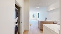 Located in Boston, MA, this modern one-bedroom, one-bathroom residence offers a thoughtfully designed layout with a clean, contemporary aesthetic throughout. Light-toned hardwood flooring flows seamlessly across the entire space, complementing the crisp white walls and creating a bright, cohesive atmosphere.

The open living area is generously proportioned, bathed in natural light and offering a clear sightline to the kitchen, which is elevated by a few steps. The kitchen is a standout feature, showcasing quartz countertops, dual islands, flat-front cabinetry in a warm wood finish paired with white upper cabinets, a subway tile backsplash, stainless steel appliances, and an undermount sink — all combining for a polished, functional workspace.

The bedroom features large black-framed windows on two walls, flooding the room with natural light and providing views of the surrounding Boston neighborhood. The spacious layout comfortably accommodates a full bedroom setup.

The bathroom is finished with large-format floor tiles, a sleek floating vanity with wood cabinetry and quartz countertop, a wall-mounted toilet, and a frameless glass sliding shower enclosure with tile surround. The overall ambiance of the residence is modern, light-filled, and move-in ready.