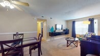 This 2-bedroom, 2-bathroom residence is thoughtfully laid out across a single floor, offering a functional and comfortable living environment. The open living and dining area forms the heart of the home, featuring plush wall-to-wall carpeting, a ceiling fan, and a textured ceiling. The living room provides ample space for seating and entertainment, with a floating media console and windows dressed in dark curtains that allow for natural light control. Adjacent to the living area, the dining space accommodates a four-person table beneath a ceiling fan with light fixture, complemented by a decorative chair rail along the walls. The galley-style kitchen is efficiently designed with white cabinetry, dark granite-style countertops, tile flooring, and black appliances including a refrigerator, range, and dishwasher. Both bedrooms are generously sized with carpeted floors and windows that bring in natural light. The primary bedroom offers a peaceful retreat, while the second bedroom provides flexibility for guests or a home office. The two bathrooms feature tile flooring and dark wood vanities; one includes a full tub-shower combination with floor-to-ceiling tile surround, while the second serves as a convenient three-piece bath.