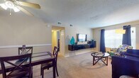 This 2-bedroom, 2-bathroom residence is thoughtfully laid out across a single floor, offering a functional and comfortable living environment. The open living and dining area forms the heart of the home, featuring plush wall-to-wall carpeting, a ceiling fan, and a textured ceiling. The living room provides ample space for seating and entertainment, with a floating media console and windows dressed in dark curtains that allow for natural light control. Adjacent to the living area, the dining space accommodates a four-person table beneath a ceiling fan with light fixture, complemented by a decorative chair rail along the walls. The galley-style kitchen is efficiently designed with white cabinetry, dark granite-style countertops, tile flooring, and black appliances including a refrigerator, range, and dishwasher. Both bedrooms are generously sized with carpeted floors and windows that bring in natural light. The primary bedroom offers a peaceful retreat, while the second bedroom provides flexibility for guests or a home office. The two bathrooms feature tile flooring and dark wood vanities; one includes a full tub-shower combination with floor-to-ceiling tile surround, while the second serves as a convenient three-piece bath.