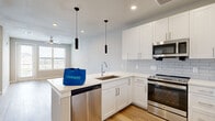 This thoughtfully designed one-bedroom, one-bathroom residence offers an efficient and modern living experience across a single floor. The open-concept kitchen and living area serves as the heart of the home, featuring crisp white shaker cabinetry, a subway tile backsplash, a peninsula island with an undermount sink, and a full suite of stainless steel appliances including a range, microwave, dishwasher, and refrigerator. Sleek pendant lighting and recessed fixtures illuminate the space, while light hardwood-style flooring and a ceiling fan in the adjoining living area enhance the airy, cohesive feel. Large windows and a glass-paneled door in the living area invite abundant natural light and provide access to outdoor views. The bedroom offers a comfortable retreat with plush carpet, a ceiling fan, and a window with views of the surrounding area. The full bathroom is finished with a white vanity, a large mirror, and wood-look flooring, and connects to a dedicated closet outfitted with built-in shelving rods for organized storage. A hallway ties the layout together efficiently. Throughout the residence, neutral tones, clean lines, and contemporary finishes create a cohesive and move-in-ready environment.