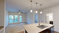 Located at 9301 Old Bee Caves Rd in Austin, TX, this single-story, 3-bedroom, 2-bathroom home offers a well-designed layout that balances comfort and functionality. The open-concept kitchen and living area serves as the heart of the home, where rich hardwood flooring transitions into plush carpeting in the living room. The kitchen is outfitted with dark espresso cabinetry, granite-style countertops, stainless steel appliances including a refrigerator, range, and microwave, and a central island with a stainless steel sink. A trio of pendant lights illuminates the island, complementing the natural light that pours in through large windows and a glass door in the living room. A ceiling fan adds to the comfort of the living area, which also opens to an outdoor view of lush greenery. The bedrooms are carpeted and bright, each featuring ceiling fans and generous windows. The primary bedroom is a comfortable size and is accompanied by a spacious walk-in closet with wire shelving. Both bathrooms are finished with granite countertops, dark cabinetry, large mirrors, and hardwood-style flooring. The primary bath includes a soaking tub. An additional walk-in closet provides ample storage throughout the home.