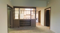 This single-floor residence offers a practical and functional layout designed for comfortable everyday living. The standout architectural feature is a bold, dark-framed open shelving unit that serves as a room divider between the carpeted living area and the kitchen, providing both visual separation and display storage while maintaining an open, connected feel throughout the space.

The kitchen is well-equipped with white appliances, including a refrigerator and a stove, complemented by light wood cabinetry that lines the walls. A skylight overhead floods the kitchen with natural light, brightening the space and adding an airy quality. The countertops and sink are positioned conveniently along the kitchen perimeter, making the layout efficient for daily use.

The living area features wall-to-wall carpeting that lends a warm, comfortable atmosphere, while the kitchen transitions to smooth, light-toned vinyl or laminate flooring for easy maintenance. A hallway visible from the main living space leads to additional rooms, offering clear circulation throughout the home. Neutral wall tones and wood-accented trim throughout contribute to a cohesive, understated aesthetic that provides a versatile backdrop for a variety of interior styles.
