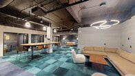 Located on Elm Street in Cincinnati, Ohio, this single-floor coworking space blends industrial architecture with contemporary design to create a dynamic and versatile work environment. The open ceiling reveals exposed ductwork, structural beams, and carefully arranged pendant and track lighting, contributing to the space's urban, loft-like character.

The main collaborative area centers around a large, oval wooden communal table surrounded by leather-backed bar stools, ideal for group work or informal meetings. Adjacent lounge zones feature a mix of tan leather sofas, neutral settees, and modern accent chairs arranged around low coffee tables, offering relaxed alternatives for focused work or conversation.

Private glass-enclosed office pods line one section of the space, providing acoustic separation while maintaining visual openness. Semi-private booth seating with upholstered banquettes and small tables offers additional options for small meetings or focused tasks. A dedicated corridor features a striking floor-to-ceiling tropical botanical mural, dramatically illuminated to serve as a bold visual focal point.

Throughout the space, a distinctive teal and charcoal patchwork carpet ties the zones together, transitioning to a slate-toned tile in the corridor. The overall ambiance balances professional functionality with creative energy, making it well-suited for a range of work styles.