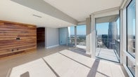Located in the heart of uptown Charlotte, this single-floor high-rise residence at 350 W 5th St offers a refined urban living experience defined by contemporary design and striking panoramic views of the city skyline. The open living area features light neutral carpeting, ceiling fans, and expansive floor-to-ceiling glass walls with sliding access to a private balcony, flooding the space with abundant natural light and framing impressive views of the Charlotte skyline.

The chef's kitchen is a standout feature, showcasing rich dark wood cabinetry with glass-front upper panels, stone countertops, a large center island with a built-in sink, stainless steel appliances including a double wall oven and built-in refrigerator, a ceramic cooktop, and a hexagonal tile backsplash. A distinctive horizontal wood-slat accent wall adds warmth and texture, visually anchoring the kitchen and living areas.

The bedrooms are carpeted and well-proportioned, each equipped with ceiling fans. One bedroom opens directly to the balcony through floor-to-ceiling sliding glass doors. A custom built-in closet system with shelving, hanging rods, and drawers provides ample storage. The bathrooms are finished with dark tile flooring, glass-enclosed walk-in showers with subway tile surround, dark wood vanities, and clean white countertops.
