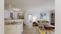 This thoughtfully designed one-bedroom, one-bathroom residence offers a functional and inviting single-floor layout. The open-concept kitchen and living area serves as the heart of the home, seamlessly connecting the two spaces. The kitchen is outfitted with white shaker-style cabinetry, a white subway tile backsplash, stainless steel appliances including a range and dishwasher, light stone countertops, and durable hardwood-style flooring that extends throughout the main living areas. Crown molding adds a refined touch to the living room, which receives generous natural light through a sliding glass door with vertical blinds leading to an outdoor area. The bedroom is a comfortable retreat featuring plush carpeting, two windows with blinds allowing ample natural light, and neutral tones that create a calm atmosphere. The full bathroom is clean and bright, appointed with white cabinetry, a single vanity with sink, and a full-size soaking tub with a shower. A hallway connects the main living spaces to the private areas of the home, contributing to an efficient and well-organized floor plan. Overall, the residence presents a cohesive, light-filled aesthetic with modern finishes throughout.