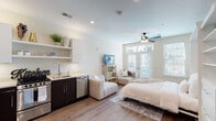 This well-designed studio unit offers a thoughtfully organized open-plan layout that maximizes every inch of available space. The main living area seamlessly integrates sleeping, lounging, and dining functions, anchored by light wood-tone flooring that flows throughout. A ceiling fan with integrated lighting provides both comfort and illumination, while a set of French doors flanked by transom windows invites generous natural light and outdoor views into the space.

The kitchen is a standout feature, equipped with stainless steel appliances including a full-size refrigerator, built-in microwave, gas range, and dishwasher. Dark lower cabinetry is paired with light countertops and open upper shelving, creating a modern, functional aesthetic. A wet bar area near the entry provides additional counter space and sink access.

A built-in Murphy bed system integrates seamlessly into the wall, accompanied by flanking shelving units and drawer storage, offering both sleeping functionality and organizational capacity without sacrificing floor space.

The bathroom is accessed via a dedicated hallway and features tile flooring, a dark-cabinet vanity with an undermount sink, a large wall mirror, and a separate walk-in shower with tile surround — delivering a clean, contemporary finish throughout.