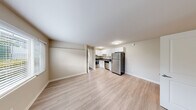 Located at 3030 NE 143rd St. in Seattle's Pinehurst neighborhood, this efficient one-bedroom, one-bathroom unit offers a thoughtfully designed single-floor layout. The open-concept living and kitchen area serves as the heart of the space, featuring light wood-style laminate flooring and neutral beige walls that create a bright, clean atmosphere. Large windows in the living area let in generous natural light and provide views of the surrounding neighborhood.

The kitchen is well-appointed with white shaker-style cabinetry, dark countertops, and a full suite of stainless steel appliances including a refrigerator, electric range, and dishwasher. A stainless steel sink and ample upper cabinet storage round out the functional cooking space.

The bedroom offers cozy wall-to-wall carpeting, a window with blinds that frames a neighborhood view, and a dedicated closet for storage. A second room with light wood-style flooring provides additional flexible living space.

The bathroom is clean and modern, featuring a white vanity with dark countertop, a large mirror, a combination tub and shower, and light wood-style flooring that ties the space together. The overall aesthetic throughout is consistent — neutral tones, white trim, and simple, functional finishes that make for a move-in ready home.