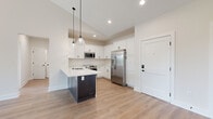 Located at 300 Dunnwood Green in Pittsford, NY, this well-appointed single-floor residence offers a thoughtfully designed layout across eight rooms. The interior is defined by light hardwood flooring throughout, crisp white walls, and vaulted ceilings that lend a sense of openness and volume to the living areas.

The kitchen serves as a functional centerpiece, featuring white shaker-style cabinetry, a dark-toned island with a built-in sink, stainless steel appliances including a refrigerator, microwave, and range, and elegant pendant lighting. The open layout connects the kitchen seamlessly to the adjacent living space.

The living and bedroom areas benefit from vaulted or elevated ceilings and generous natural light. One room opens directly to a private balcony through sliding glass doors, offering peaceful views of surrounding mature trees. A spacious walk-in closet with wire shelving provides ample storage.

The two bathrooms are finished with dark espresso-toned vanities, white quartz countertops, large wall mirrors with vanity lighting, and neutral stone-look tile flooring. One bathroom features a dual-sink vanity, adding a practical touch.

Throughout the space, clean lines, a neutral color palette, and quality finishes create a modern yet inviting atmosphere suited to comfortable everyday living.