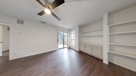 This well-designed one-bedroom, one-bathroom single-story residence offers a functional and cohesive layout across its compact footprint. Dark hardwood-style flooring flows consistently throughout the space, providing a warm, unified aesthetic that complements the crisp white walls found in every room.

The living room serves as the central gathering space, featuring a ceiling fan with light fixture, a textured ceiling, and a sliding glass door that opens to an outdoor patio, flooding the area with natural light. A built-in shelving unit and lower cabinetry with countertop space add practical storage and display options along one wall.

The kitchen is efficiently arranged in a galley-style configuration, outfitted with white shaker cabinetry, white quartz-style countertops, a subway tile backsplash, a stainless steel sink, a dishwasher, and an electric range. Upper and lower cabinets maximize storage within the space.

The bedroom is a comfortably sized private retreat, featuring its own ceiling fan, a window with outdoor views, and a louvered closet door, maintaining the clean, neutral palette found throughout the unit.

The bathroom is finished in all-white with a full tub-shower combination, a toilet, and brushed nickel fixtures, offering a clean and functional design. Overall, the space presents a bright, move-in-ready interior with consistent finishes throughout.