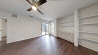This well-designed one-bedroom, one-bathroom single-story residence offers a functional and cohesive layout across its compact footprint. Dark hardwood-style flooring flows consistently throughout the space, providing a warm, unified aesthetic that complements the crisp white walls found in every room.

The living room serves as the central gathering space, featuring a ceiling fan with light fixture, a textured ceiling, and a sliding glass door that opens to an outdoor patio, flooding the area with natural light. A built-in shelving unit and lower cabinetry with countertop space add practical storage and display options along one wall.

The kitchen is efficiently arranged in a galley-style configuration, outfitted with white shaker cabinetry, white quartz-style countertops, a subway tile backsplash, a stainless steel sink, a dishwasher, and an electric range. Upper and lower cabinets maximize storage within the space.

The bedroom is a comfortably sized private retreat, featuring its own ceiling fan, a window with outdoor views, and a louvered closet door, maintaining the clean, neutral palette found throughout the unit.

The bathroom is finished in all-white with a full tub-shower combination, a toilet, and brushed nickel fixtures, offering a clean and functional design. Overall, the space presents a bright, move-in-ready interior with consistent finishes throughout.