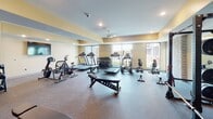 Located in Inver Grove Heights, MN, this well-appointed fitness center offers a comprehensive workout environment across a single open floor. The space is divided into two functional zones: a cardio area and a strength training area, seamlessly connected for a cohesive exercise experience.

The cardio zone features multiple treadmills, elliptical machines, a stationary bike, and rowing machines, all positioned near large windows that flood the area with natural light and provide views of the surrounding exterior. A wall-mounted flat-screen television adds entertainment options for cardio sessions, and a ceiling fan promotes air circulation throughout.

The strength training area is equipped with a power rack, weight plates, adjustable benches, a cable machine, and resistance bands, catering to a wide range of exercise routines. Floor-to-ceiling mirrors line one wall, enhancing the sense of space while allowing users to monitor their form. Rubber-floored surfaces provide durability and safety underfoot throughout both zones.

Additional amenities include a dumbbell rack with a full range of free weights and a water fountain station conveniently located near the entrance. Recessed lighting and warm yellow-toned walls contribute to an energizing yet comfortable ambiance, making this fitness center a fully equipped resource for residents of the community.