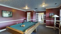 Located at 5400 Beverly Hills Dr in Columbus, Ohio, this single-floor property offers a well-appointed interior with distinctive design elements throughout. The standout feature of the space is a dedicated game room, finished with deep burgundy walls accented by crisp white chair-rail molding and crown molding that frame the room with a classic, polished look. A full-size pool table with a green felt surface serves as the centerpiece, making the space ideal for entertainment and recreation. The room is finished with dark carpeting that complements the rich wall tones, and a textured ceiling with flush-mount light fixtures provides warm, even illumination. French-style glass-panel doors connect the game room to adjoining areas, allowing natural light to filter through while maintaining a sense of defined space. The layout flows openly into adjacent hallways and rooms, suggesting a thoughtfully organized floor plan. Overall, the space combines a welcoming, functional atmosphere with classic interior details, offering a comfortable and versatile environment suited for both everyday living and hosting guests.