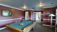Located at 5400 Beverly Hills Dr in Columbus, Ohio, this single-floor property offers a well-appointed interior with distinctive design elements throughout. The standout feature of the space is a dedicated game room, finished with deep burgundy walls accented by crisp white chair-rail molding and crown molding that frame the room with a classic, polished look. A full-size pool table with a green felt surface serves as the centerpiece, making the space ideal for entertainment and recreation. The room is finished with dark carpeting that complements the rich wall tones, and a textured ceiling with flush-mount light fixtures provides warm, even illumination. French-style glass-panel doors connect the game room to adjoining areas, allowing natural light to filter through while maintaining a sense of defined space. The layout flows openly into adjacent hallways and rooms, suggesting a thoughtfully organized floor plan. Overall, the space combines a welcoming, functional atmosphere with classic interior details, offering a comfortable and versatile environment suited for both everyday living and hosting guests.