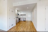 Located at 141 South Harrison Street in East Orange, NJ, this thoughtfully designed studio unit makes efficient use of its single-floor layout. The open-plan kitchen and living area form the heart of the space, with warm wood-look flooring running throughout and crisp white walls that enhance the sense of brightness. The kitchen is outfitted with a full suite of stainless steel appliances — including a refrigerator, electric range, over-the-range microwave, and dishwasher — complemented by sleek white upper cabinetry, wood-toned lower cabinets, and a marble-effect backsplash with matching quartz-style countertops. The living area receives natural light through a large multi-pane window fitted with roller shades, offering views of the surrounding neighborhood. A dedicated closet provides storage, while an in-unit laundry area adds everyday convenience. The bathroom is a standout feature, finished with large-format porcelain floor tiles, a floating wood-grain vanity with an illuminated medicine cabinet mirror, a full bathtub with shower, and a striking mosaic stone accent wall that adds texture and warmth. Recessed lighting and clean, neutral finishes give the entire unit a contemporary, move-in-ready appeal.