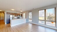 Located at 515 E Market St in the heart of Indianapolis, this well-appointed one-bedroom, one-bathroom unit offers a thoughtfully designed open-concept floor plan finished with light hardwood-style flooring throughout. The combined kitchen and living area serves as the centerpiece of the home, bathed in natural light from a generous bank of windows framing views of the surrounding cityscape. The kitchen is equipped with rich dark wood cabinetry, stainless steel appliances including a refrigerator, range, and microwave, and a sleek white peninsula with an integrated sink — ideal for both everyday cooking and casual entertaining. The living area extends to a private balcony accessible through sliding glass doors, offering open urban views. A long hallway connects the main living space to the private quarters, lined with two closets providing ample storage. The bedroom is a calm, light-filled retreat with its own walk-in closet featuring wrap-around shelving and hanging rods. The full bathroom features a dark wood vanity with white countertop and wood-toned tile flooring, maintaining a consistent modern aesthetic. A dedicated laundry room with full-size washer and dryer rounds out the functional amenities of this well-designed urban residence.