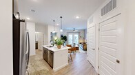 This thoughtfully designed 1-bedroom, 1-bathroom residence offers a seamless open-concept layout that maximizes every square foot. Light wood-tone flooring flows throughout the entire space, creating a warm and cohesive aesthetic.

The kitchen is a standout feature, showcasing a large quartz waterfall island with seating, a herringbone tile backsplash, stainless steel appliances — including a French door refrigerator, electric range, and built-in microwave — and a dual-tone cabinet design pairing crisp white uppers with wood-finish lowers. Pendant lighting above the island adds a stylish, modern touch.

The open living room benefits from natural light pouring in through French doors, which lead to an outdoor balcony. A ceiling fan, recessed lighting, and ample wall space complete the relaxed yet refined atmosphere.

The bedroom is a serene retreat with a dedicated window for natural light, ceiling fan, and direct access to a generously sized walk-in closet outfitted with multi-tier wire shelving systems for organized storage.

The bathroom features wood-finish cabinetry with matte black hardware, granite countertops, and a clean, modern design. The layout is efficient and well-appointed throughout, offering both functionality and contemporary style.