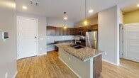 Located at 721 N Phillips Ave in Sioux Falls, South Dakota, this single-floor unit offers a contemporary, open-concept design with a thoughtful layout and quality finishes throughout. The main living area is anchored by light-toned luxury vinyl plank flooring that extends through the kitchen and common spaces, creating a cohesive and easy-to-maintain surface. A sliding glass door leads to a private balcony, flooding the living space with natural light and providing views of the surrounding neighborhood.

The kitchen is a standout feature, showcasing rich dark-stained cabinetry, a tile backsplash, stainless steel appliances including a refrigerator, range, and microwave, and a granite-topped island with a dual-basin sink. Pendant lighting above the island adds warmth and definition to the space. An open pantry area provides additional storage convenience.

The carpeted bedrooms are well-proportioned, each featuring large sliding windows that bring in natural light and street-level views of the urban surroundings. Ceiling fans add comfort and functionality. The bathroom includes a full tub-shower combination with clean white tile surround and brushed nickel fixtures. A dedicated utility area houses the water heater, HVAC system, and in-unit laundry, keeping mechanical essentials neatly contained.