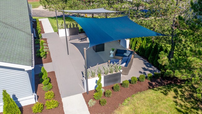 Take in this spectacular aerial view of our outdoor lounge, nestled under the expansive blue and grey sail shades - offers the ultimate relaxation spot. Surrounded by lush, meticulously manicured landscaping, it's your perfect retreat. - Atlas North