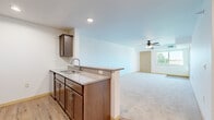 This single-floor residence offers a practical and cohesive layout across three bedrooms and two bathrooms. The open-concept kitchen flows directly into the living room, separated by a peninsula countertop with a granite-style surface and a double-basin sink — an ideal setup for both everyday living and entertaining. The kitchen is equipped with stainless steel appliances, including a refrigerator, range, and microwave, all complemented by rich dark wood cabinetry and light wood-style vinyl flooring. The living room is carpeted and features a ceiling fan with integrated lighting, along with a window that allows natural light to filter in and offers a view of greenery outside. Each of the three bedrooms is carpeted and features clean white walls, natural light from windows, and closet space — the primary bedroom includes a dedicated closet with a hanging rod. The two bathrooms maintain the same design language as the rest of the home, with matching dark wood vanities, white countertops, and light wood-style vinyl flooring. One bathroom includes a tub-shower combo, while the other features a longer vanity layout. Overall, the space presents a clean, neutral, and functional interior with consistent finishes throughout.