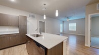 This well-appointed single-floor residence in San Antonio, Texas offers three bedrooms and two bathrooms with a thoughtfully designed open-concept layout. The kitchen serves as the heart of the home, showcasing a large center island with a granite-style countertop, undermount sink, and pendant lighting overhead. Dark wood cabinetry lines the walls, complemented by black appliances including a refrigerator, range, and built-in microwave. Light hardwood-style flooring extends seamlessly from the kitchen into the adjacent living area, which features a ceiling fan and windows that invite natural light. The bedrooms are carpeted for comfort, each equipped with ceiling fans and window blinds, providing a quiet and cozy retreat. The primary bedroom offers a generous footprint with ample wall space. The two bathrooms are finished with matching dark wood vanities, granite-style countertops, and large mirrors. One bathroom features a tiled soaking tub and shower combination with a marble-inspired surround, while the other offers a clean, functional vanity setup with light wood-tone flooring. A dedicated closet provides additional storage. The neutral color palette throughout creates a cohesive, modern aesthetic suited to a variety of interior styles.