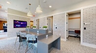 This thoughtfully designed single-floor space blends functionality with contemporary style across a compact but well-utilized footprint. The layout accommodates two dining areas, a dedicated office, a bedroom, and two laundry rooms, making it a versatile environment suited for both work and daily living.

The dining areas are visually striking, featuring whitewashed brick accent walls, pendant lighting with cream-colored dome fixtures, and built-in tables with integrated power outlets. Carpeted floors add warmth, while a wall-mounted TV serves as a central focal point. Natural light filters in through windows, offering views of surrounding architecture.

The office area is designed for productivity, with a private room featuring a bold red herringbone tile accent wall, a wall-mounted display screen, a long conference table, quilted black leather chairs, and framed abstract artwork. A separate individual workstation with a built-in desk, white brick surround, and a red accent wall provides a focused, quieter alternative.

The bedroom is compact yet functional, efficiently utilizing its space. Throughout the space, a cohesive design palette of neutral tones, textured brick surfaces, warm wood elements, and patterned carpeting creates a polished, modern ambiance.