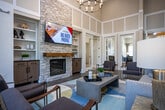 Located at 810 Tapestry Way in Knoxville, Tennessee, this single-floor community clubhouse is thoughtfully designed with upscale finishes and a cohesive, nature-inspired aesthetic throughout. The main lounge commands attention with soaring ceilings, white paneled wainscoting, and an abundance of natural light streaming through large windows and glass doors that open to an outdoor patio. A stacked-stone fireplace with a wood mantel and built-in shelving serves as a striking focal point, while a statement chandelier anchors the space elegantly. A dedicated dining nook features a grid of decorative lantern-style wall sconces, creating a dramatic and intimate atmosphere alongside round tables and patterned upholstered chairs. The bar and social area is distinguished by a reclaimed wood ceiling and accent wall, patterned tile backsplash, a long white quartz island with bar seating, and a full beverage station with a wine fridge. Lush living green walls add a vibrant, organic element to this gathering space. The business center offers workstations, computers, printing capabilities, and a comfortable seating area, accented by nature-themed artwork and textured botanical wallcoverings. Throughout the clubhouse, large-format tile flooring, curated artwork, and cohesive neutral tones with blue accents create a welcoming and refined environment.