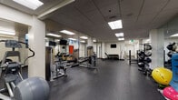 Located at 1109 West Main Street in Boise, Idaho, this fitness facility offers a comprehensive workout environment designed to accommodate a wide variety of training styles and fitness goals. The space is laid out on a single floor with an open, expansive floor plan that promotes ease of movement between workout zones.

The facility features durable rubber flooring throughout, providing safety and comfort during exercise. Structural columns punctuate the space and help define distinct training areas without compromising the overall openness of the room. A drop ceiling with recessed panel lighting ensures consistent, bright illumination across the entire floor.

The strength training area is well-appointed with a Rogue power rack, barbell stations with plate storage, a comprehensive dumbbell rack, kettlebells, and multiple cable and selectorized machines suited for targeted muscle group training. Large mirrors line sections of the walls, enhancing spatial awareness and allowing users to monitor their form.

The cardio zone includes treadmills and an elliptical trainer, accompanied by wall-mounted televisions for entertainment. Additional functional training equipment such as TRX suspension trainers, medicine balls, stability balls, and plyo boxes rounds out the facility's offerings.

The overall ambiance is clean, functional, and purposefully designed, making this a versatile fitness space well-suited for both individual and group training sessions.