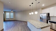 This thoughtfully designed 1-bedroom, 1-bathroom residence offers a comfortable and functional layout across a single floor. The heart of the unit is the open-concept living, dining, and kitchen area, where a central granite-topped island serves as both a prep space and casual gathering point. The kitchen is outfitted with crisp white shaker cabinetry, a classic subway tile backsplash, stainless steel appliances including a refrigerator with ice maker, range, and built-in microwave, and granite countertops that carry through the space cohesively. A dedicated pantry provides additional storage directly off the kitchen. Globe pendant lights hang above the island, adding a modern design touch. Wood-look flooring runs throughout the entire unit, lending a clean and contemporary aesthetic. The living area is brightened by natural light and features a ceiling fan. The bedroom is a comfortable size, offering a walk-in closet with wire shelving, a ceiling fan, and access to natural light through multiple windows. A second closet with open shelving adds further storage versatility. The full bathroom includes a granite vanity with white cabinetry and a tub-shower combination. A dedicated laundry area and utility room round out the practical offerings of this well-equipped space.
