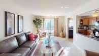 This two-story home offers a practical and comfortable layout designed to accommodate everyday living with ease. The main level features a welcoming living room with plush carpeting, a leather sofa, and a glass coffee table centered on a patterned area rug. Natural light streams in through sliding glass doors that open to an outdoor deck, creating a bright and airy atmosphere. A staircase with a classic wrought-iron railing connects the two floors, adding a subtle architectural detail to the space. Adjacent to the living area, the kitchen is outfitted with warm oak cabinetry, granite-style countertops, a stylish mosaic tile backsplash, and black appliances including an electric range, making it both functional and visually appealing. The full bathroom on the lower level features a wood-framed vanity mirror, a single-basin sink with oak cabinetry below, and a shower-tub combination. Upstairs, the bedrooms are carpeted and filled with natural light from well-placed windows that offer views of surrounding greenery. One bedroom is thoughtfully designed with mirrored sliding closet doors that enhance the sense of space, while another features a large window with charming pink curtains and a classic white dresser. Together, the rooms create a warm and inviting home environment.