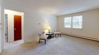 Located at 24 Monadnock in Keene, New Hampshire, this single-floor residence offers a straightforward and functional layout designed for comfortable everyday living. The living room is generously proportioned, featuring wall-to-wall carpeting, neutral cream-toned walls, and multiple windows that invite an abundance of natural light while offering views of the surrounding neighborhood. Baseboard heating runs along the perimeter, ensuring efficient warmth throughout the colder New England seasons. Additional carpeted rooms provide flexible spaces well-suited for use as bedrooms or a home office, each brightened by windows and finished with clean, light-colored walls. The kitchen is equipped with classic wood cabinetry, a coil-burner electric range with overhead ventilation, a stainless steel sink, and ample counter space, delivering a practical cooking environment. The full bathroom features tile flooring, warm wood cabinetry with overhead storage, a vanity with a white countertop, and a tub-shower combination enclosed by a striped curtain. Throughout the unit, the consistent use of neutral tones, soft carpeting, and natural light creates a calm and welcoming ambiance, making this a practical and comfortable home in the heart of Keene.