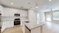 Located at 350 Bay Laurel Dr in Saint Augustine, Florida, this well-appointed 2-bedroom, 2-bathroom single-story home offers a clean, modern design with thoughtful finishes throughout. The open-concept kitchen is a standout feature, showcasing crisp white shaker cabinetry, granite countertops, a large center island with an undermount sink, and a full suite of stainless steel appliances including a refrigerator, electric range, over-the-range microwave, and dishwasher. Elegant pendant lighting and recessed ceiling lights illuminate the space, which flows naturally into the living area over light wood-style flooring. The bedrooms are carpeted for comfort, with the primary bedroom offering a ceiling fan and generous proportions, complemented by its own en-suite bathroom. The primary bath features a dual-sink vanity with granite countertops, white cabinetry, and a large mirror, creating a bright and functional retreat. The secondary bedroom is similarly well-sized with natural light from double windows and a ceiling fan. Two dedicated closets provide ample storage, including a walk-in closet with wire shelving. Neutral tones, clean lines, and consistent finishes throughout give this home a fresh, move-in-ready appeal.