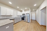 Located at 15037 Tahoma Blvd SE in Yelm, Washington, this single-story, 3-bedroom, 2-bathroom home offers a well-organized and efficiently designed layout. Light-toned luxury vinyl plank flooring flows consistently throughout, complemented by warm wood-trimmed baseboards and doors that add a clean, cohesive aesthetic.

The combined kitchen and living area serves as the heart of the home. The kitchen is outfitted with white upper cabinetry, gray lower cabinets, granite-look countertops, a peninsula for additional workspace, and a full suite of stainless steel appliances including a refrigerator, range, microwave, and dishwasher. Recessed lighting illuminates the space throughout. The living area benefits from natural light through large windows with views of surrounding greenery, and includes a wall-mounted mini-split system for climate control.

The three bedrooms are comfortably sized, with the primary bedroom offering generous space. The secondary bedrooms feature windows that bring in natural light. Both bathrooms include granite-look vanities and LVP flooring, with one bathroom featuring a sliding glass door shower enclosure. A dedicated laundry room houses a full-size washer and dryer. A hallway and closet complete the functional layout of this tidy, move-in ready home.