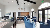 Located at 2510 West Ranch in Carlsbad, this stylish lounge is a thoughtfully designed single-floor communal space that seamlessly blends comfort with modern elegance. The interior is anchored by dramatic vaulted ceilings accented with bold black exposed beams, lending the space a grand, airy feel. Large arched windows and glass-paneled doors invite abundant natural light, enhancing the open and welcoming ambiance throughout.

A fully equipped kitchen bar serves as the functional centerpiece of the space, featuring dark cabinetry, a striking textured brick backsplash, a built-in refrigerator, and a coffee station. A sleek white countertop runs along the bar, complemented by a row of warm-toned wooden barstools that add a touch of rustic contrast to the contemporary design.

The lounge area is furnished with plush blue velvet armchairs arranged around a round accent table, creating an inviting setting for conversation or relaxation. Decorative wire pendant lights hang in a cluster above, adding an artistic focal point to the high ceiling. Light-toned tile flooring runs throughout, contributing to the bright, clean aesthetic. Additional shelving and accent décor complete the space, making the West Ranch Lounge a well-appointed destination for residents and guests alike.