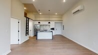 This contemporary 1-bedroom, 1-bathroom loft at 250 Greene Street in New Haven, Connecticut offers a thoughtfully designed open-concept layout with striking architectural details throughout. The main living and kitchen area impresses with soaring ceilings and a dramatic mezzanine level accessed by a sleek black ladder, adding vertical dimension and a true loft character to the space. Wide-plank light oak hardwood flooring runs seamlessly throughout, complementing the clean, neutral palette of white walls and crisp trim.

The chef's kitchen serves as the centerpiece of the open floor plan, anchored by a substantial island clad in dark veined stone countertops and fitted with a sink. Flat-front white cabinetry extends to the ceiling, while a marble-look tile backsplash, stainless steel appliances—including a French door refrigerator and built-in microwave—complete the modern aesthetic. Pendant lighting adds a warm, focused glow above the island. A wall-mounted mini-split system provides efficient climate control.

The bedroom is generously proportioned, featuring large black-framed windows that frame lush tree canopy views, filling the room with abundant natural light. The bathroom is finished with a clean white quartz vanity, modern brushed hardware, and a full-width mirror. Every detail reflects a refined, minimalist sensibility suited for contemporary urban living.