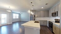 Located at 1412 E Mockingbird Ln in Midland, Texas, this well-designed single-story unit offers a clean, contemporary aesthetic throughout. The open-concept layout seamlessly connects the kitchen, dining, and living areas, all finished with rich, dark hardwood-style flooring that adds warmth and continuity to the space.

The kitchen is a standout feature, showcasing gray shaker-style cabinetry with ample storage, crisp white quartz countertops, a subway tile backsplash, and a full suite of stainless steel appliances including a refrigerator, range, and microwave. A generously sized center island with an undermount sink serves as both a functional workspace and a casual gathering point, accented by elegant glass globe pendant lights overhead.

The living area is bright and open, benefiting from natural light through multiple windows, and is equipped with a ceiling fan for added comfort. Bedrooms offer plush carpeting, ceiling fans, and windows that invite natural light, creating a relaxing retreat.

The bathrooms are thoughtfully finished, with one featuring a tiled tub-surround combination and gray vanity cabinetry, while another showcases a sleek walk-in shower with floor-to-ceiling tile and a frameless sliding glass door. Throughout the unit, neutral tones and modern finishes create a cohesive, move-in-ready environment.