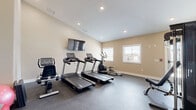 Located at 2525 Crescent Cove Dr in Evans, Colorado, this single-room fitness center offers a well-organized and fully equipped exercise space designed to support a range of workout routines. The room features durable rubber flooring suited for high-traffic use, warm neutral-toned walls, and recessed lighting throughout the ceiling, creating a clean and functional atmosphere.

The cardio section is outfitted with multiple Spirit-brand treadmills, an elliptical trainer, a recumbent bike, and a rowing machine, providing ample options for aerobic exercise. A wall-mounted flat-screen television is positioned for easy viewing during workouts. On the strength training side, the space includes a multi-station cable machine, an adjustable weight bench, a rack of dumbbells in varying weights, medicine balls, and a stability ball, offering a comprehensive free-weight and resistance training setup.

Natural light enters the room through several windows along the exterior wall, offering views of the surrounding neighborhood. A glass-panel entry door provides additional brightness and convenient access. The high ceiling height adds to the sense of openness within the space. Overall, this fitness center is efficiently laid out to maximize usability while maintaining an uncluttered, accessible environment for residents.