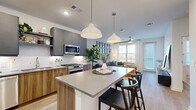 Located at 652 Angier Ave NE in Atlanta's Old Fourth Ward neighborhood, this single-floor residence showcases a thoughtfully designed, contemporary interior with a cohesive aesthetic throughout. The open-concept kitchen and living area serve as the heart of the home, anchored by a generous quartz-topped island with seating for casual dining. The kitchen is outfitted with two-tone cabinetry — warm wood-grain lower cabinets paired with matte grey uppers — complemented by a marble-look tile backsplash and a full suite of stainless steel appliances, including a gas range, French door refrigerator, built-in microwave, and dishwasher. Pendant lighting and light wood-style flooring enhance the modern, inviting atmosphere. The adjacent living room is bright and airy, featuring large windows that draw in generous natural light and offer views of the Atlanta skyline, with a ceiling fan adding comfort overhead. The primary bedroom features a striking accent wall, ceiling fan, and large windows, while the secondary bedroom is finished in crisp white tones with natural light. The bathroom presents a sleek grey vanity with quartz countertop, framed mirror, and contemporary globe lighting. A private balcony extends the living space outdoors with open city views.