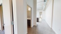 This single-story space combines industrial and modern design elements to create a versatile, open environment. The architecture is immediately distinguished by its soaring exposed ceiling structure, complete with visible ductwork, steel trusses, and track lighting that contribute to an airy, loft-like atmosphere throughout the main living areas.

Polished concrete floors run throughout much of the space, lending a sleek, contemporary aesthetic that complements the bright white walls. The kitchen is well-appointed, featuring stainless steel appliances including a full-size range with over-the-range microwave and a large side-by-side refrigerator. Two-tone cabinetry pairs dark wood lower cabinets with light gray upper cabinets, accented by white countertops and a subway tile backsplash.

Two bathrooms serve the space. One features a combination tub and shower with classic white subway tile surround, a dark-cabinet vanity, and polished concrete floors. The second bathroom offers a glass-enclosed walk-in shower with matching tile, a modern floating vanity with a large mirror, and consistent concrete flooring.

A carpeted room with floor-to-ceiling glass sliding doors provides an abundance of natural light and direct exterior access. The overall ambiance is clean, modern, and adaptable to a variety of uses.