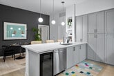 Located at 2590 Red Hill Ave in Santa Ana, CA, this thoughtfully designed one-bedroom unit offers a well-appointed layout across a single floor. The open-concept kitchen and living area serves as the heart of the space, anchored by a striking waterfall-edge quartz island with an integrated sink and seating. Soft gray shaker cabinets with brass hardware extend floor-to-ceiling, providing abundant storage, while stainless steel appliances and globe pendant lighting complete the contemporary aesthetic. Light wood-tone flooring flows throughout, tying the spaces together seamlessly. The living room features a bold charcoal accent wall, large windows with sheer drapery, and direct access to an outdoor area, allowing natural light to fill the room. A ceiling fan adds practicality to the comfortable lounge area. The generously sized primary bedroom offers a calming retreat with dual design perspectives — one side features crisp white walls with natural light from a street-facing window, while the other presents a sophisticated dark accent wall with wall-mounted lighting. A dedicated walk-in closet with full shelving and hanging systems provides excellent organization. A separate room with bold black-and-white botanical wallpaper and light wood flooring adds a distinctive, versatile space ideal for a home office or reading nook.