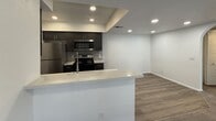 This single-floor apartment spans 740 square feet and offers a well-organized layout comprising two bedrooms, one bathroom, a kitchen, an entrance, and a hallway. The unit features a modern kitchen equipped with dark espresso cabinetry, white quartz countertops, a subway tile backsplash, and stainless steel appliances including a refrigerator, microwave, and electric range. Recessed lighting illuminates the kitchen and adjacent living area, which is defined by a peninsula-style breakfast bar. Wood-look flooring runs throughout the main living spaces, providing a clean, contemporary aesthetic. The primary bedroom measures 220 square feet and features carpet flooring and a closet. The second bedroom is also carpeted and includes a window with outdoor views, allowing natural light to fill the room. A notable architectural detail is an arched doorway visible in the hallway, adding a subtle design accent to the interior. The bathroom is fitted with a full tiled walk-in shower unit with grab bars, providing both functionality and accessibility. Throughout the unit, neutral white walls and consistent finishes create a cohesive and move-in-ready environment.