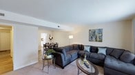 Located at 2029 Bedford St in Durham, North Carolina, this two-story residence offers a thoughtfully arranged floor plan that balances functionality with comfort. The main living area is open and inviting, anchored by a spacious living room with plush carpeted flooring and neutral wall tones that create a warm, welcoming atmosphere. A large sectional sofa arrangement centers the room, complemented by glass-topped accent tables that add a contemporary touch. A decorative art piece adorns the wall, contributing to the space's polished aesthetic. The living area flows seamlessly into a dedicated dining space, which comfortably accommodates a round dining table and chairs — ideal for both casual meals and entertaining guests. Just beyond the dining area, the kitchen is visible and benefits from natural light, with access to appliances including a refrigerator. The open-concept design between the living, dining, and kitchen zones enhances the sense of spaciousness and promotes easy movement throughout the main level. Recessed ceiling details and neutral finishes throughout the main floor lend a clean, cohesive look. With two floors, the home provides ample space for both living and private quarters, making it a well-rounded residence in the Durham area.