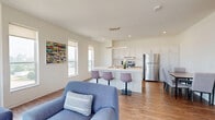 Located at 1009 S 10th St in Sheboygan, Wisconsin, this well-appointed 2-bedroom, 1-bathroom residence offers a thoughtfully designed single-floor layout with a clean, contemporary aesthetic throughout. The open-concept living and kitchen area serves as the heart of the home, where warm hardwood-style flooring flows seamlessly underfoot. Large windows flood the living room with natural light while framing impressive elevated views of the surrounding Sheboygan cityscape. The kitchen is outfitted with white shaker-style cabinetry, light wood lower cabinets, stainless steel appliances including a full-size refrigerator and range, and a central island with bar seating — ideal for both cooking and casual dining. A dedicated dining area with ample space adjoins the kitchen. The spacious primary bedroom features plush carpeting, a sliding closet, and an additional walk-in closet area, providing generous storage. The second bedroom is equally bright and comfortable. The full bathroom is clean and accessible, featuring a walk-in shower with grab bars and hardwood-style flooring. An in-unit laundry room with a stacked washer and dryer adds everyday convenience, completing this modern and functional residence.