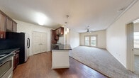 This efficiently laid-out 1-bedroom, 2-bathroom single-floor unit offers a thoughtful design that maximizes both comfort and functionality. The open-concept kitchen and living area forms the heart of the home, where rich dark wood cabinetry, dark granite-style countertops, a tile backsplash, and stainless steel appliances lend a polished look to the kitchen. A breakfast bar peninsula provides additional counter space and serves as a natural divider between the kitchen and the living area. The living room is warm and inviting, featuring plush carpeting, a ceiling fan, and elegant French doors that allow abundant natural light and provide outdoor access. The bedroom is a comfortable retreat, complete with soft carpet, a ceiling fan with light fixture, and a window with views to the outside. The two bathrooms are clean and functional, with one featuring a full soaking tub and shower combo, a single vanity with dark countertop, white cabinetry, and wood-style flooring. Throughout the unit, neutral cream-toned walls, six-panel doors, and consistent finishes create a cohesive and welcoming atmosphere. A double-door closet off the living area provides ample storage.