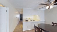 This single-floor residence offers a functional and well-organized layout designed for comfortable everyday living. The kitchen serves as a central feature of the home, showcasing white upper and lower cabinetry that maximizes storage while maintaining a clean, bright aesthetic. A peninsula-style countertop with a gas cooktop and sink extends into the living area, creating an open, connected feel that also provides space for casual dining or meal prep. The white countertops and light-toned walls contribute to an airy atmosphere throughout the kitchen. Adjacent to the kitchen, a dining area comfortably accommodates a table and chairs, making it an ideal spot for meals and gatherings. A hallway connects the main living area to the rest of the home, where additional rooms can be glimpsed in the background, hinting at a practical floor plan. Tile flooring runs through the kitchen and connecting spaces, offering durability and easy maintenance. The textured ceiling adds a subtle layer of detail throughout. Overall, the space presents a straightforward, move-in-ready environment with a neutral color palette that provides a versatile backdrop for a variety of interior styles.