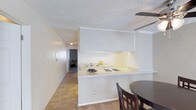 This single-floor residence offers a functional and well-organized layout designed for comfortable everyday living. The kitchen serves as a central feature of the home, showcasing white upper and lower cabinetry that maximizes storage while maintaining a clean, bright aesthetic. A peninsula-style countertop with a gas cooktop and sink extends into the living area, creating an open, connected feel that also provides space for casual dining or meal prep. The white countertops and light-toned walls contribute to an airy atmosphere throughout the kitchen. Adjacent to the kitchen, a dining area comfortably accommodates a table and chairs, making it an ideal spot for meals and gatherings. A hallway connects the main living area to the rest of the home, where additional rooms can be glimpsed in the background, hinting at a practical floor plan. Tile flooring runs through the kitchen and connecting spaces, offering durability and easy maintenance. The textured ceiling adds a subtle layer of detail throughout. Overall, the space presents a straightforward, move-in-ready environment with a neutral color palette that provides a versatile backdrop for a variety of interior styles.