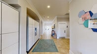Located at 1005 S Fork Village Dr in Cramerton, NC, this single-floor community clubhouse offers a well-appointed gathering space spanning a generously sized footprint. The entry corridor welcomes visitors with light tile flooring, recessed lighting, crown molding, and a modern package locker system, setting a clean and organized tone throughout.

The main living area is a standout, featuring soaring vaulted ceilings and floor-to-ceiling windows that flood the space with abundant natural light and offer views of the surrounding community. Comfortable seating arrangements, including sofas and accent chairs in neutral and aqua tones, create an inviting atmosphere for socializing. Wainscoting details and arched doorways add architectural character throughout.

Adjacent to the living area is a fully functional kitchen outfitted with rich cherry wood cabinetry, granite countertops, black appliances, and tile flooring. A dedicated coffee and snack bar counter provides a convenient amenity for residents.

The fitness center is well-equipped with hardwood floors and large windows providing natural light. It features a comprehensive range of cardio machines — including treadmills, recumbent bikes, and a rowing machine — as well as strength training equipment, offering residents a complete workout experience. A corridor with interior windows connects the fitness area to the main hallway, maintaining visual openness throughout the facility.